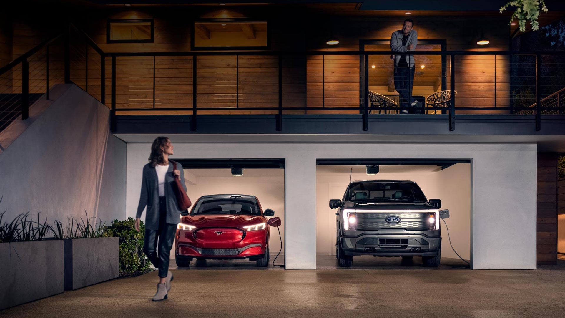 Woman walking out from home garage with a 2024 Mustang® Mach-E and Ford Lightning® truck in plugged-in and charging | Hutcheson Ford Sales in Saint James MO